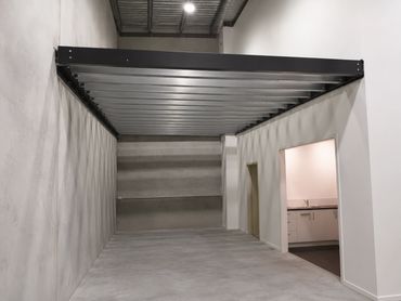 Empty industrial room with a mezzanine and a kitchen area.