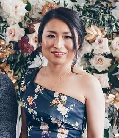 Woman in floral dress posing against a flower wall.