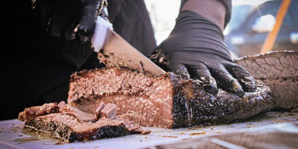Close-up of a hand slicing smoked brisket with a knife.