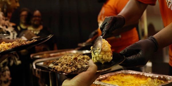 A person serving food at a buffet line with black gloves.
