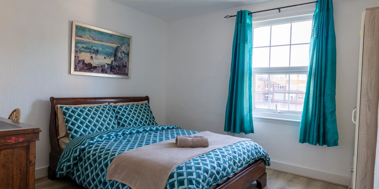 A bedroom with a bed, a window, and a painting on the wall