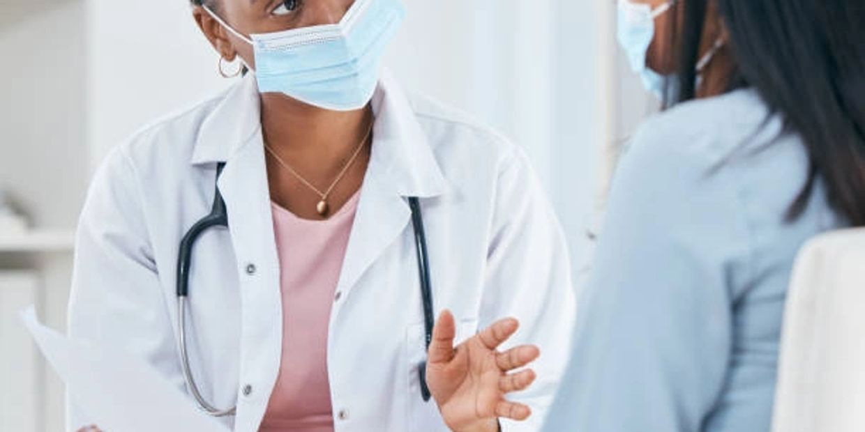 Doctor wearing a mask consulting a patient in a clinical setting.