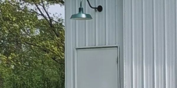A white metal building with a closed door and green outdoor lamp.