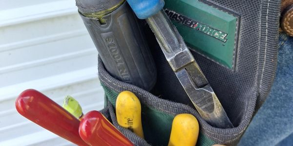 Close-up of a hand tool pouch with pliers and a screwdriver inside.
