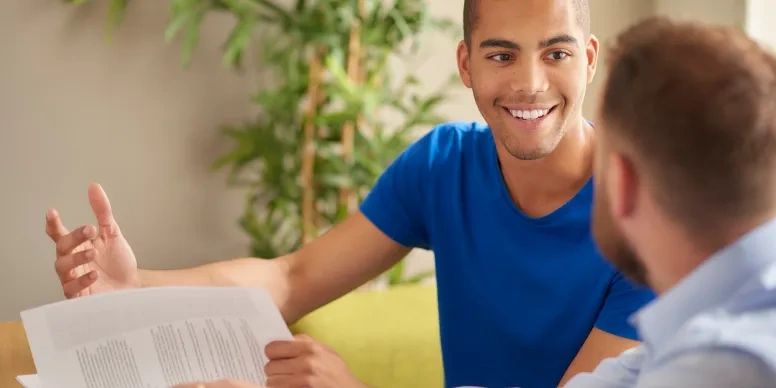 Young BIPOC man reviewing his research paper with a professor.