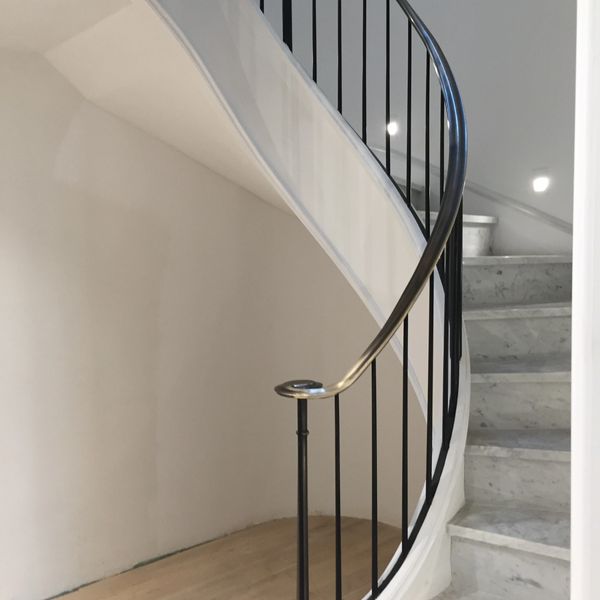 Curved staircase with vertical pickets and custom brushed metal rail cap