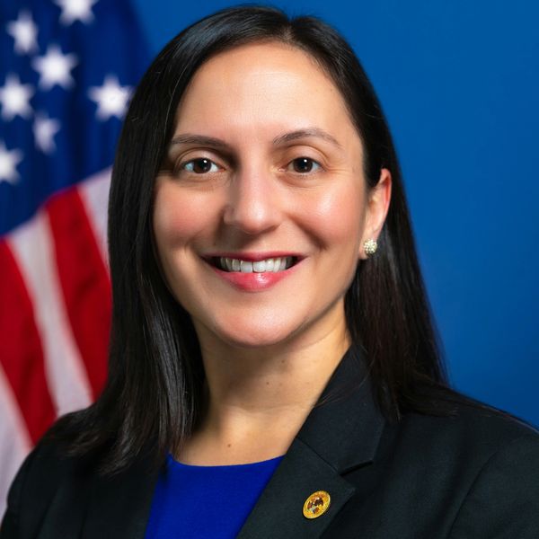 Photo of Barbara Barreno-Paschall in front of the United States flag wearing a black blazer and blue