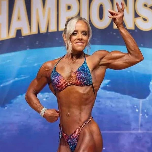 Female bodybuilder posing confidently on stage in a colorful bikini.