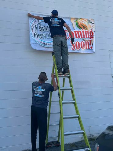 A person putting up Main Munchery's coming soon sign on outside wall