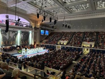 A large audience watches a formal event in a grand auditorium.