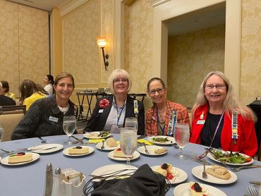 Four women sitting at a round table with plates of salad and dessert, smiling.