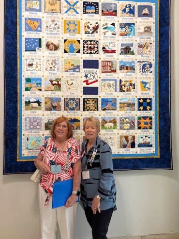 Two women standing in front of a colorful quilt representing U.S. states.