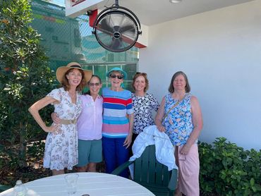 Five women enjoying a sunny day outdoors, smiling and posing for a photo.