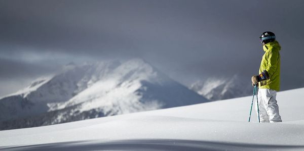 Skier in bright green jacket standing on snowy mountain slope under cloudy sky.