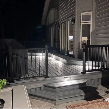 Well-lit backyard deck with stairs and railing at night.