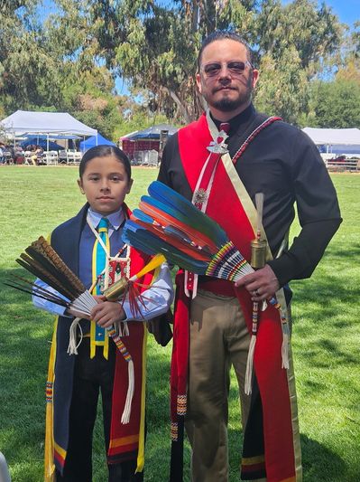 Indigenous Man with Son Gourd Dancers on the lawn with event tents in the background.