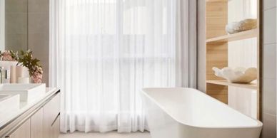 Minimalist bathroom with a white freestanding tub and sheer curtains.