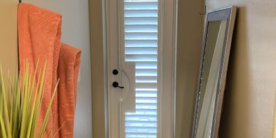 A white door with vertical blinds, an orange chair, and a large mirror leaning against the wall.