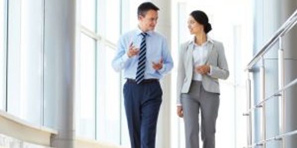 Two business professionals walking and talking in a bright office corridor.