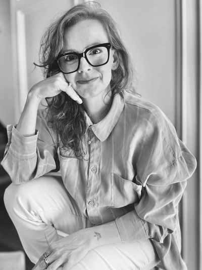 Woman with glasses, smiling and resting her face on her hand in a casual pose.
