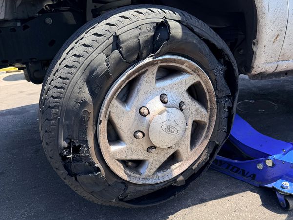 Severely damaged tire on a Ford vehicle with a blue jack underneath.