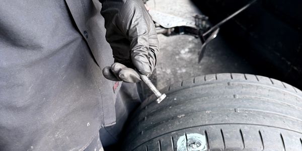 Person wearing gloves holding a bolt near a worn-out tire.