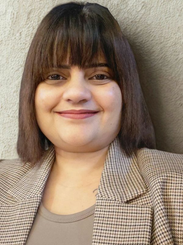 Smiling woman with straight hair and bangs wearing a checked blazer.