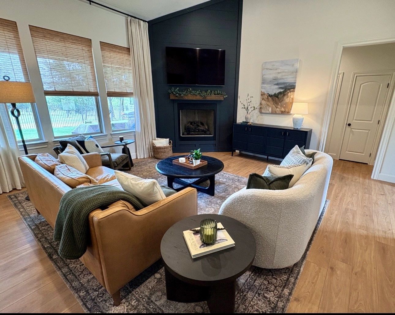 Bright living room with black fireplace, floor-to-ceiling curtains, woven shades, curated furniture,