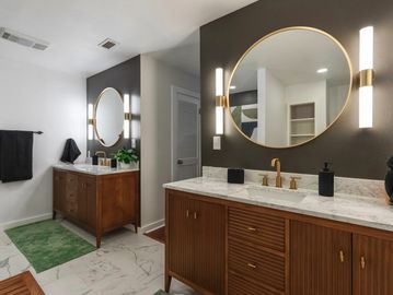 Modern bathroom with wooden vanities, round mirrors, and marble countertops.