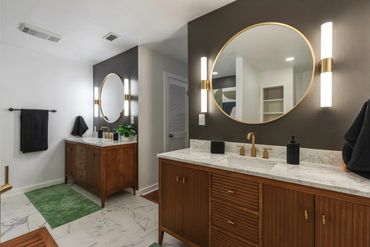 Elegant bathroom with wood cabinets, round mirrors, and marble countertops.