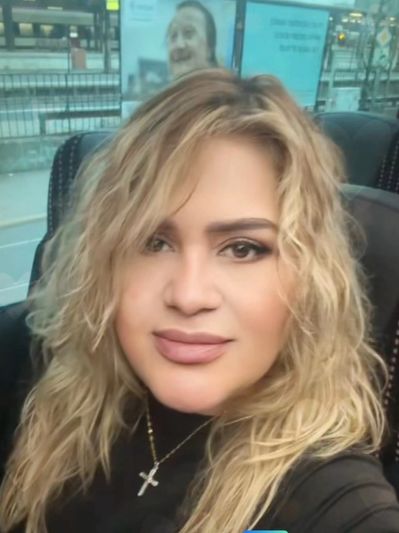 Woman with blonde hair and cross necklace smiling on a bus.