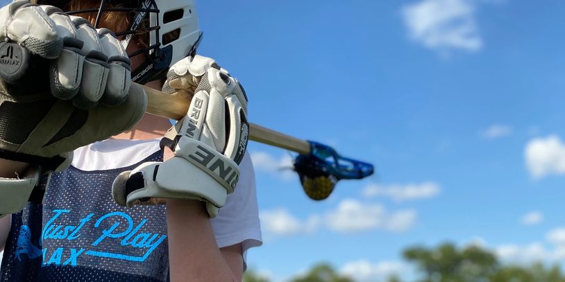 Young athlete holds lacrosse stick, ready to play under blue sky.