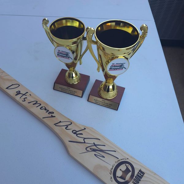 Two gold trophies and a signed wooden paddle on a table.