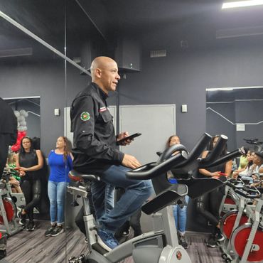 Man on stationary bike in gym surrounded by people watching.