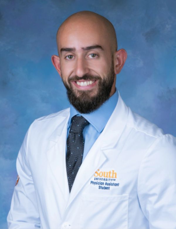 Smiling man in a white coat and blue shirt.