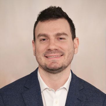 Man smiling in a suit jacket and white shirt.