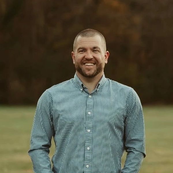 Smiling man in a checkered shirt outdoors.