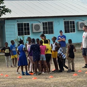 A group of children and adults gather outdoors near a building for an activity.