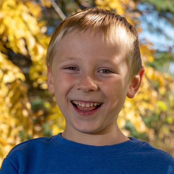 Caucasian boy smiling in dappled sunlight with yellow leaf background.