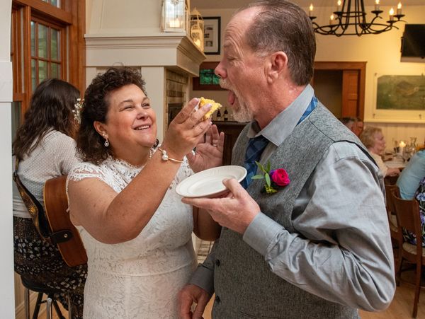 Bride in wedding gown feeding cake to groom at a reception.