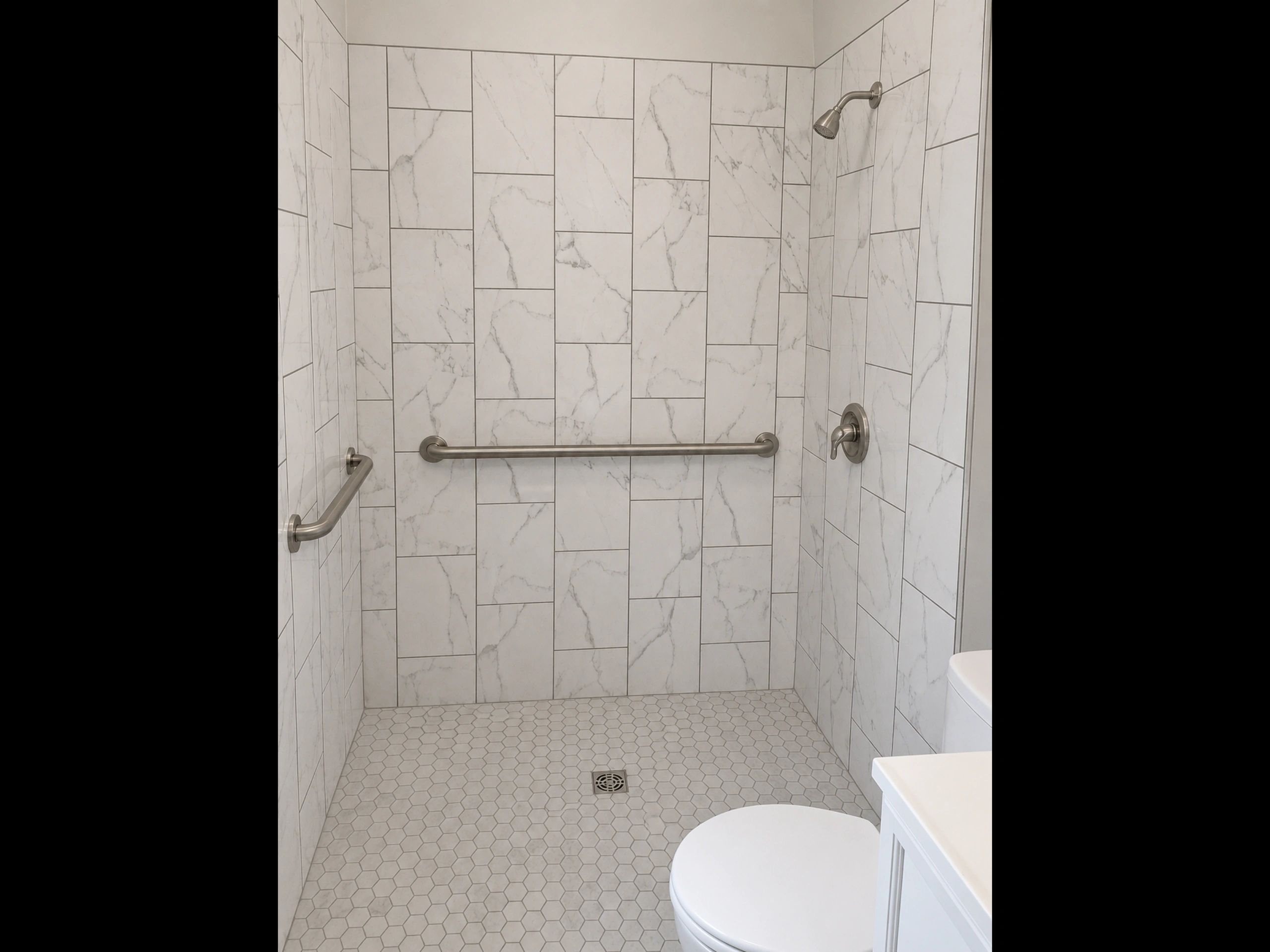 Modern tiled shower with grab bars and a handheld showerhead.