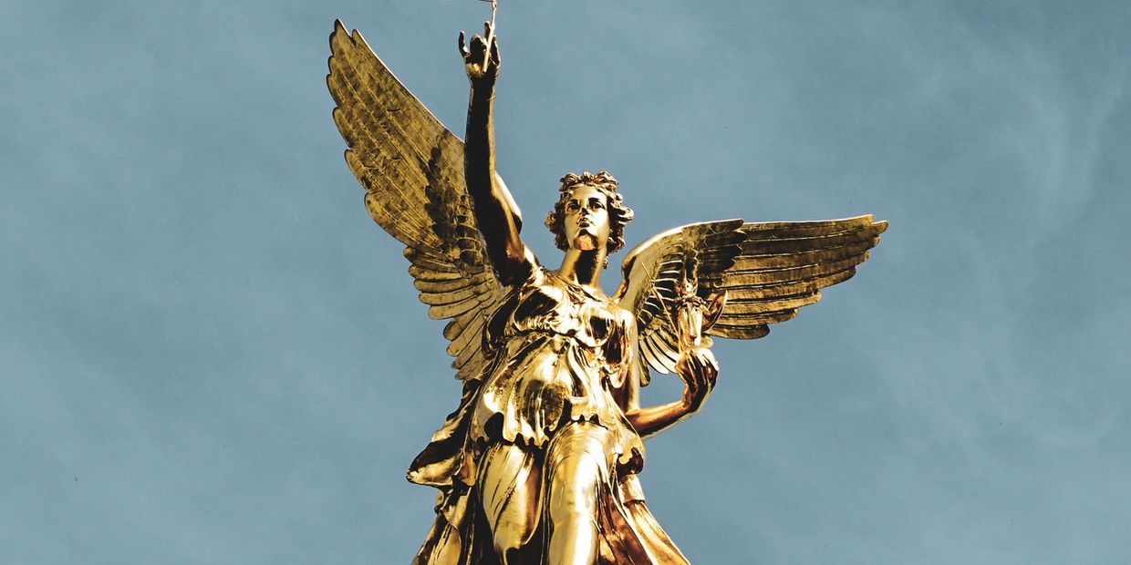 Looking up at a golden angel statue with the blue sky above.