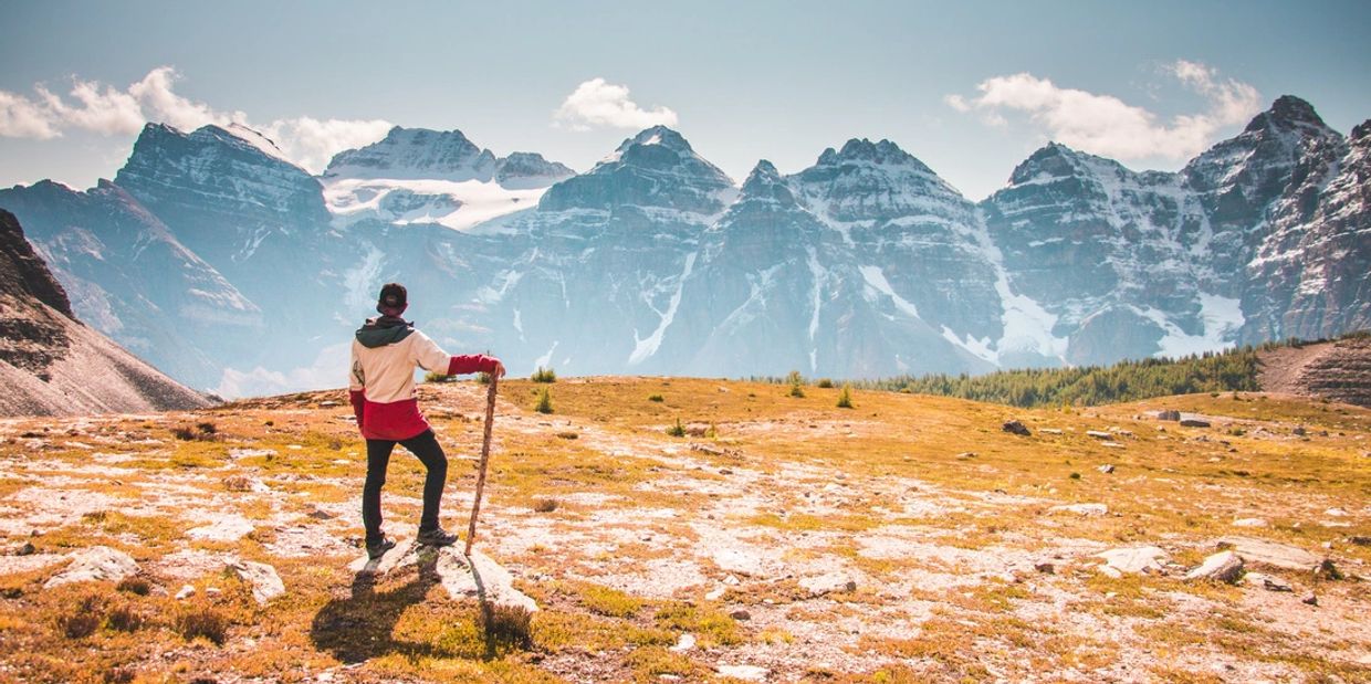 A hiker with hiking stick looks out to mountains in the distance. 