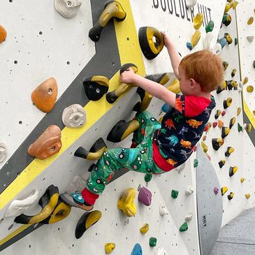 toddler climbing on an indoor bouldering wall in active clothing