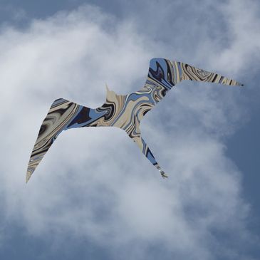 A bird-shaped object with a marbled pattern flying against the cloudy sky.