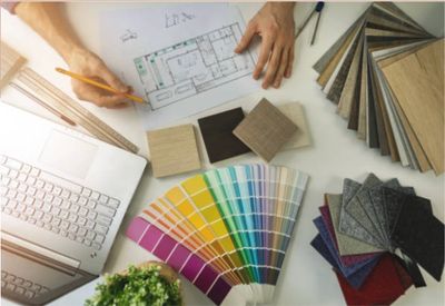 Person designing a floor plan surrounded by color swatches and wood samples.
