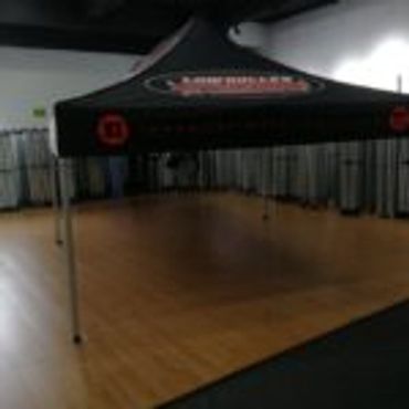 Black canopy tent set up indoors on wooden flooring.