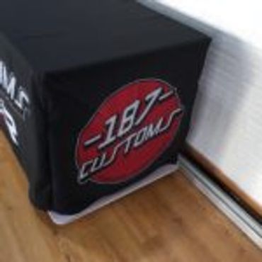 Black fabric cover with a red circle and white text reading '187 Custom' on a wooden floor.