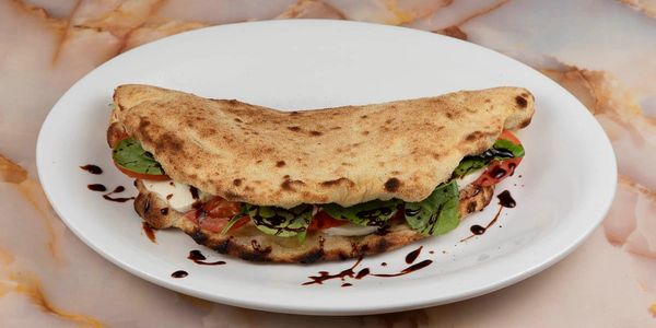 Grilled flatbread sandwich with fresh greens and tomato on a white plate.