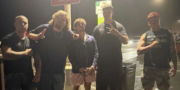 Five men posing under streetlights with drinks lined up on the ground at night.